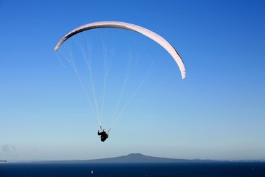  A paraglider at Shakespear Regional Park appears to be gliding over Rangitoto